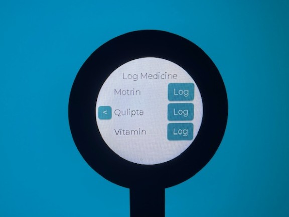 The medication screen photographed with the round back device. It has a header which reads 'Log Medicine' and then lists 'Motrin', 'Qulipta', and 'Vitamins'. Each is next to a button which reads 'Log'.