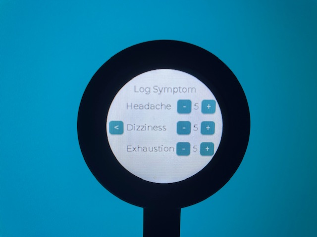 The symptoms screen photographed with the round back device. It has a header which reads 'Log Symptom' and then lists 'Headache', 'Exhaustion', and 'Dizziness'. Each is next to a a value label and + / - buttons to allow the user to change the severity